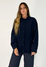 Camisa de corte oversize en color azul marino, confeccionada en tejido de algodón con textura tipo pana. Presenta cuello clásico, cierre frontal con botones al tono y mangas largas con puños abotonados.