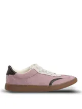 Championes de estilo urbano en color lila, confeccionados en material sintético con textura similar a la gamuza. Presentan detalles en color marrón oscuro en la puntera y el talón, cordones claros y suela de goma color caramelo.