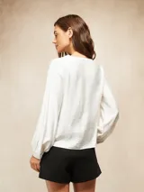 Blusa de color blanco hueso con escote en V y cierre frontal de botones pequeños. Presenta mangas largas con puños ajustados y un diseño de corte recto.
