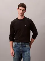 Remera de manga larga negra de corte holgado, con cuello redondo y el logo monograma de Calvin Klein bordado en blanco en el pecho.
