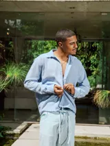 Camisa de lino rayada en tonos celeste y blanco, con cuello y botones frontales. Presenta un estampado en el frente y la espalda.