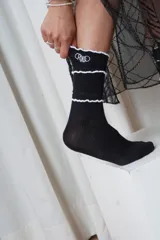 Medias blancas de caña media con tejido acanalado, detalles de volados negros en el puño y bordado con la palabra "Criado" en color negro.