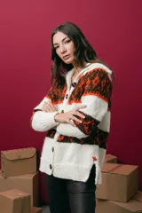 Saco tejido a mano con diseño jacquard, de corte recto y largo a la cadera. Presenta cuello redondo, cierre frontal con botones y mangas largas. Incluye tajos laterales en el ruedo.