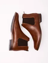 Botín tipo Chelsea de cuero sintético color marrón, con paneles elásticos laterales oscuros y suela de goma con pequeño tacón.