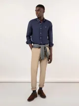 Camisa azul de hombre confeccionada en 100% algodón twill, tintada en prenda. Cuenta con corte regular fit, cuello button-down, cierre frontal de botones, manga larga con puño simple y pequeño logo rojo bordado en el pecho.