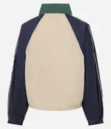 Campera rompeviento de diseño tricolor con bloques de color en verde, beige y blanco. Presenta cuello alto, cierre frontal con cremallera, mangas raglán y puños ajustados. El ruedo incluye un cordón regulable para un ajuste personalizado.