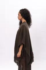 Ruana de tejido de punto color marrón chocolate, con diseño envolvente, cuello en V y detalle de flecos en el ruedo. Incluye etiqueta de cuero sintético con el logo de la marca en la parte frontal.