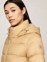 Campera puffer color beige, con capucha y cierre frontal con cremallera. Tiene dos bolsillos delanteros con botón a presión y parche con el logo de Tommy Hilfiger en la manga.
