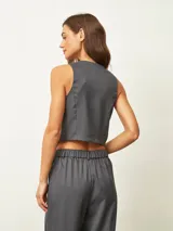 Chaleco de sastrería gris oscuro con diseño de rayas verticales finas, escote en V y cierre frontal con tres botones. Presenta un corte entallado y bolsillos decorativos en la parte inferior.