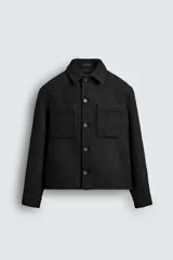 Sobrecamisa de corte relajado en tejido de textura bouclé color negro. Presenta cuello clásico, cierre frontal con botones, mangas largas con puños abotonados y dos bolsillos de plastrón en el pecho.