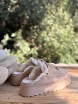 Suecos de símil gamuza color beige, con interior forrado en corderito sintético, plataforma y detalle de tira frontal con cordones y punteras metálicas.
