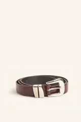 Cinturón de cuero liso en color bordó, con hebilla metálica plateada y pasador metálico decorativo.