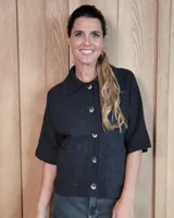 Cardigan de punto color negro, con cuello camisero, cierre frontal de botones y mangas cortas con terminación acanalada. Presenta bolsillos frontales tipo parche.