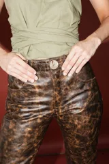 Pantalón de cuero color marrón con estampado abstracto, corte acampanado y abertura en el ruedo.