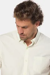 Camisa lisa de manga corta color crema, confeccionada en 100% algodón, con cuello abotonado y un bolsillo en el pecho.