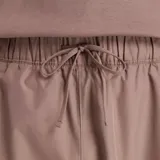 Pantalón deportivo New Balance de tejido técnico color marrón topo, con cintura elástica ajustable con cordón, bolsillos laterales con cierre y cordón de ajuste en el dobladillo. Presenta un pequeño logo gráfico en la pierna izquierda.