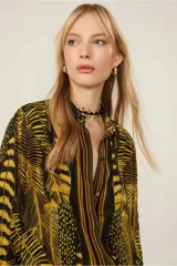 Camisa de viscosa estampada con diseño de plumas en tonos amarillo y negro. Tiene cuello clásico, mangas largas con puños abotonados, cierre frontal con botones y corte tradicional.