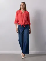 Blusa blanca de gasa marca Zac & Rachel, con cuello a la base, escote en V, abertura central con botones, bolsillo aplicado en el pecho y mangas largas regulables con presilla y botón. Tiene terminación opcional de nudo en el ruedo.