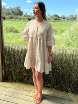 Vestido corto de lino color beige claro, con cuello mao, escote con botones de nácar, mangas tres cuartos con volados y ruedo con volado.
