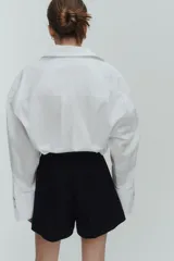 Short negro de tiro alto con pliegues tableados, bolsillos al bies y corte holgado.