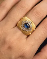Anillo de bronce con baño de oro, diseño texturizado en relieve con detalles ornamentales y piedra central azul zafiro.