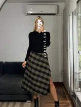 Pollera midi de corte recto con tajo lateral, confeccionada en tela con estampado escocés en tonos marrones, blancos y negros.