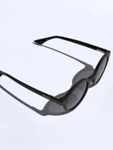 Lentes de sol con marco redondo de color negro, con detalle de línea roja en las patillas y logo de la marca grabado. Cuentan con cristales oscuros polarizados con protección UV 400.