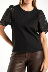 Remera de algodón peinado color negro, con mangas cortas de broderie con diseño calado y terminación festoneada. Presenta un corte oversize y cuello redondo.