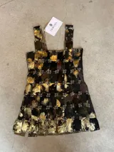 Vestido corto de diseño de autor, confeccionado mediante una estructura de piezas rectangulares de cuero pintadas a mano en tonos negro y dorado, unidas entre sí por argollas metálicas. Presenta un diseño sin mangas con breteles anchos y una silueta recta.