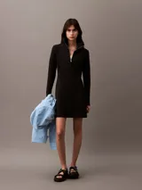 Vestido corto negro de neopreno de algodón, con cuello alto y cierre frontal de cremallera. Tiene mangas largas, corte entallado y falda con vuelo. Incluye un bordado de Calvin Klein en el pecho.