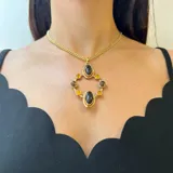 Collar con cadena de eslabones dorados y dije colgante de diseño geométrico en bronce. El dije presenta dos óvalos centrales de nácar y está rodeado por ocho cuentas pequeñas de perla o piedra blanca, engastadas en aros de bronce.