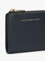 Billetera compacta Tommy Hilfiger de material sintético con textura granulada, cierre superior con cremallera metálica dorada y logo de la marca grabado en el frente.