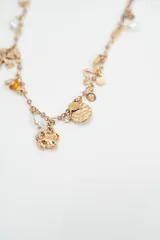 Set de dos collares con dijes variados. El primero cuenta con una cadena de perlas blancas y dijes metálicos que incluyen un cactus, cerezas rojas, un corazón y una luna. El segundo collar presenta una cadena dorada con cuentas pequeñas y dijes metálicos con formas de corazón, flores y elementos geométricos.