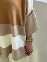 Poncho de punto con diseño de rayas horizontales en tonos tierra, blanco y beige. Presenta un corte holgado, cuello redondo y mangas anchas con puños acanalados.