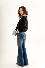 Jean estilo oxford de tiro medio, color negro, con recortes curvos en las piernas y botones decorativos en la botamanga.