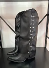 Botas de caña alta negras con punta en pico, taco bajo y detalles metálicos plateados en los laterales de la caña.