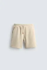 Bermuda de algodón color beige, estilo jogger, con corte relajado, cintura elástica ajustable con cordón y bolsillos laterales y trasero.