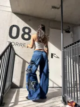Pantalón jeans azul de corte wide leg, tiro medio y diseño holgado, con grandes aplicaciones de estrellas negras desgastadas en los laterales de las piernas.