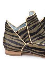 Botines de piel con diseño original, confeccionados artesanalmente en España. Presentan un estampado animal print en tonos verde y negro, con una estructura de piezas superpuestas y una pieza frontal elevada que estiliza el empeine. Cuentan con cierre lateral, interior forrado en piel y suela de cuero.