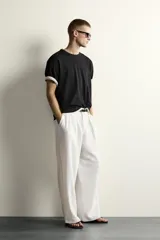 Pantalón relaxed fit de color blanco off-white, confeccionado en tejido con lino. Cuenta con pliegues frontales en la cintura, bolsillos delanteros y cierre frontal con cremallera y botón.