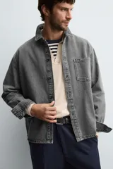Camisa de denim de algodón, color gris oscuro lavado, de corte holgado (boxy fit). Presenta cuello solapa, manga larga con puño abotonado, bolsillo de plastrón en el pecho y cierre frontal con botones.