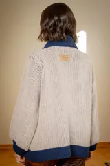 Campera de punto tipo cárdigan con cierre frontal de doble cursor, confeccionada en lana. Presenta un diseño bicolor con cuerpo en tono gris claro y detalles en azul marino en el cuello, la franja central, los bolsillos y los puños. Posee mangas largas con terminación ajustada y bolsillos frontales.