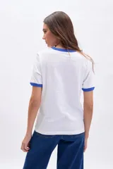 Remera blanca de manga corta con cuello redondo y ribete en color azul. Presenta un estampado central en azul con texto en francés que hace referencia a una dirección en París.