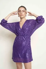 Vestido corto de lentejuelas color violeta, con escote en V cruzado, mangas tres cuartos abullonadas y ajuste en la cintura.