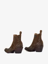 Bota corta estilo cowboy de cuero gamuzado color marrón oscuro, con punta afilada y tacón ancho y alto. Presenta bordados decorativos en hilo turquesa en el empeine y el lateral.