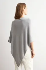 Capa tejida en hilo de lurex color beige, con cuello bote y diseño asimétrico de corte fluido.