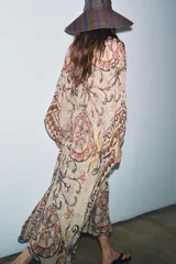 Vestido tipo túnica de viscosa con escote en pico y mangas tipo capa. Presenta un diseño estampado con motivos ornamentales en tonos tierra, beige y rosado, con pliegues en la cintura y bajo asimétrico.