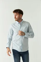 Camisa celeste de manga larga con logo bordado y bolsillo en el pecho.