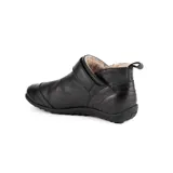 Botita baja Marcel confeccionada en cuero vacuno color marrón, con interior de corderito ultrasuave. Presenta costuras pespunteadas decorativas, tira lateral con hebilla metálica dorada y detalles de elástico negro. Suela plana de goma negra.