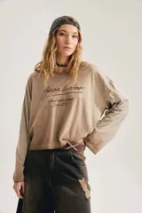 Remera oversize de manga larga color tostado con efecto gastado, cuello redondo y estampado frontal con tipografía manuscrita.